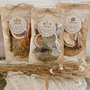 May include: Three kraft paper bags tied with twine, each containing dried herbs and spices. The bags are labeled "Golden Glow", "Forest Spice", and "Fall Harvest". The "Golden Glow" bag includes calendula, orange, vanilla, and cinnamon. The "Forest Spice" bag includes eucalyptus, bay leaves, and juniper berries.