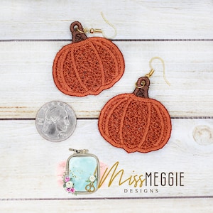 Puede incluir: Un par de pendientes de color naranja en forma de calabaza con tallos marrones y ganchos dorados. Los pendientes están hechos de fieltro y tienen aproximadamente el tamaño de una moneda de 25 centavos de dólar estadounidense.