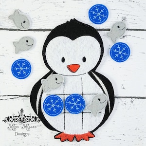 Puede incluir: Un juguete de pingüino de fieltro con un cuerpo blanco y negro, un pico naranja y patas naranjas. El pingüino tiene una cuadrícula en su vientre con círculos azules de copo de nieve y formas de peces grises. Hay círculos azules de copo de nieve y formas de peces grises adicionales alrededor del pingüino.