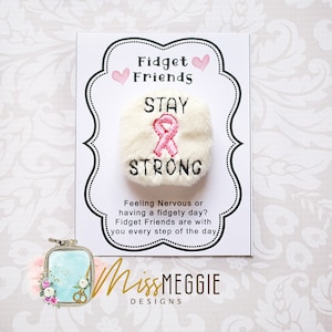 Peut inclure: Jouet de fidget en peluche blanche avec un ruban rose brodé et le texte "STAY STRONG" sur une carte blanche avec le texte "Fidget Friends" et "Feeling Nervous or having a fidgety day? Fidget Friends are with you every step of the day." et le texte "MissMEGGIE DESIGNS".