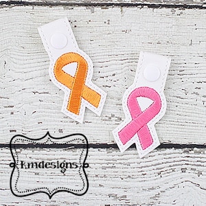 May include: Two white fabric keychains with a button closure. One keychain features a pink ribbon and the other features an orange ribbon. Both ribbons are embroidered.