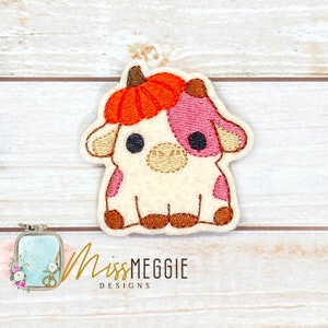 May include: Embroidered patch of a white cow with pink spots wearing a small orange pumpkin hat. The cow is sitting with its legs tucked under its body.