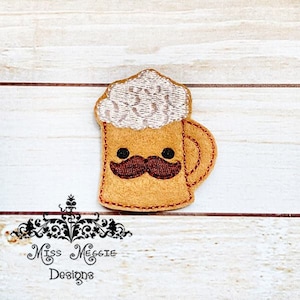 Puede incluir: Una aplicación de fieltro de una jarra de cerveza con espuma y bigote. La jarra es marrón con espuma blanca y bigote marrón. La jarra tiene una cara feliz con dos ojos negros.