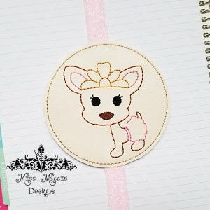 May include: A white felt circle with a pink ribbon attached. The circle has an embroidered image of a white dog wearing a gold crown and a pink bow. The dog is looking to the right. The text "Miss Maggie Designs" is below the circle.