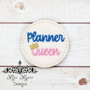 May include: A white felt circle with blue and pink embroidery that reads "Planner Queen" with a gold crown above the word "Queen".