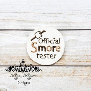 May include: White embroidered patch with a brown outline. The patch features a stick figure holding a marshmallow on a stick and the text "Official S'more Tester".
