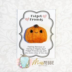 May include: An orange pumpkin-shaped fidget toy with a smiling face, part of the "Fidget Friends" collection. The card also features the text "Feeling Nervous or having a fidgety day? Fidget Friends are with you every step of the day."