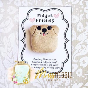 Puede incluir: Una tarjeta blanca con el texto "Fidget Friends" y un corazón rosa a cada lado del texto. Un pequeño perro de peluche marrón con nariz y lengua rosas está en la tarjeta. El texto debajo del perro dice "Feeling Nervous or having a fidgety day? Fidget friends are with you every step of the way." El texto "Miss Meggie Designs" está en la parte inferior de la tarjeta.