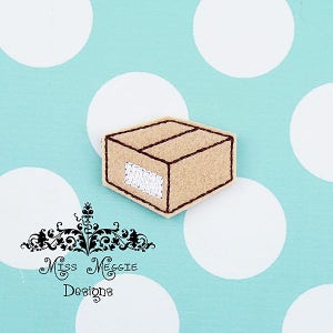 Könnte beinhalten: Eine hellbraune Filzbox mit braunen Stichlinien und einem weißen, gestickten Etikett. Die Box befindet sich auf einem hellblauen Hintergrund mit großen weißen Punkten. Der Text "Miss Meggie Designs" ist ebenfalls sichtbar.