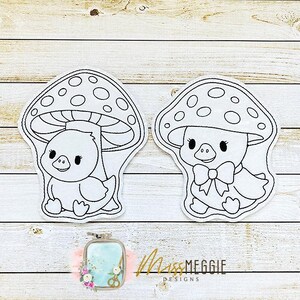 May include: Two white and black embroidered patches. Each patch features a duckling under a mushroom. One duckling has a bow tie. The patches are on a light wood grain background. The text "Miss Meggie Designs" is in the lower right corner.