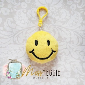 Peut inclure: Porte-clés en peluche jaune en forme de smiley avec un sourire brodé noir. Le porte-clés est attaché à une boucle en plastique jaune.