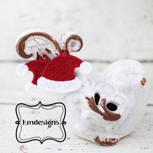 Puede incluir: Pendientes de crochet de gorro de Papá Noel rojo y blanco. Los pendientes cuelgan de una figurita de pájaro de cerámica blanca. Los pendientes están hechos a mano y tienen un pompón blanco en la parte superior del gorro.