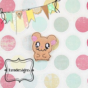 May include: A brown and pink embroidered cartoon hamster with big eyes and a smile. The hamster is sitting on a white background with a polka dot pattern.