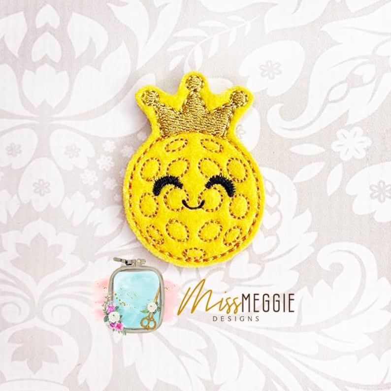 May include: A yellow felt pineapple with a gold crown and a smiling face. The pineapple is decorated with a stitched pattern of circles.