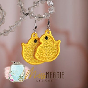 May include: A pair of yellow embroidered ghost-shaped earrings with black eyes. The earrings are hanging from silver hooks.