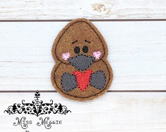 May include: Brown felt applique of a cartoon animal holding a red heart. The animal has black eyes, a gray nose, and pink cheeks.
