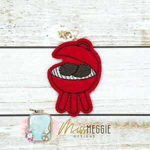 May include: A red felt barbecue grill applique with black accents and two brown food items inside. The applique has a black stitched outline and three legs. The text "Miss MEGGIE DESIGNS" is visible in the lower right corner.