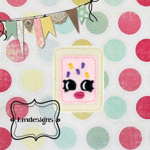 May include: A pink and white felt applique of a smiling, cartoon-style pop tart with purple and yellow sprinkles. The applique is surrounded by a white border.