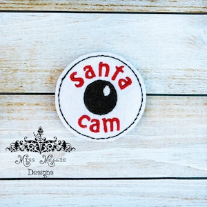 May include: White round patch with red embroidered text "Santa Cam" and a black embroidered eye in the centre.