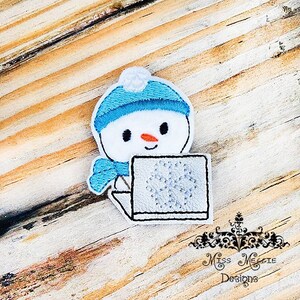 May include: A blue and white snowman with a blue hat and scarf is using a laptop with a snowflake design. The snowman is on a wood background.