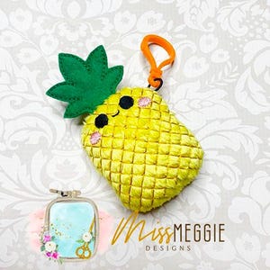 May include: A yellow pineapple plush toy with a green leafy top and a smiling face. The pineapple has a small orange loop attached to the top, suggesting it is a keychain.