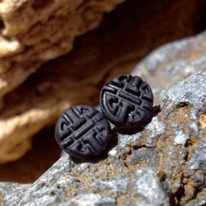 May include: Two black stud earrings with a geometric design. The earrings are made of a smooth, black material and have a raised, intricate pattern.