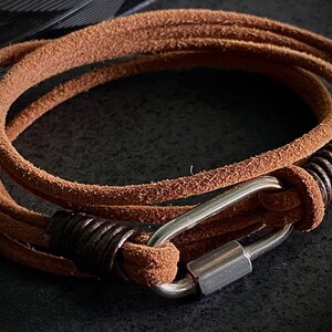 May include: A brown leather wrap bracelet with a silver carabiner clasp and a brown leather wrap detail.