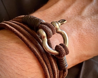May include: A brown leather bracelet with a silver clasp. The bracelet is made of multiple strands of leather that are woven together.