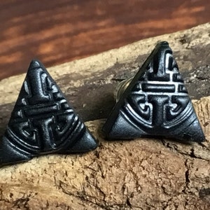 May include: A pair of black triangle-shaped earrings with a geometric design. The earrings are made of metal and have a shiny finish.
