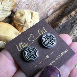 May include: A pair of silver earrings with a circular design featuring a knot pattern. The earrings are displayed on a brown card with the text "Ukr Art" and "m/shop/UkrHeart".