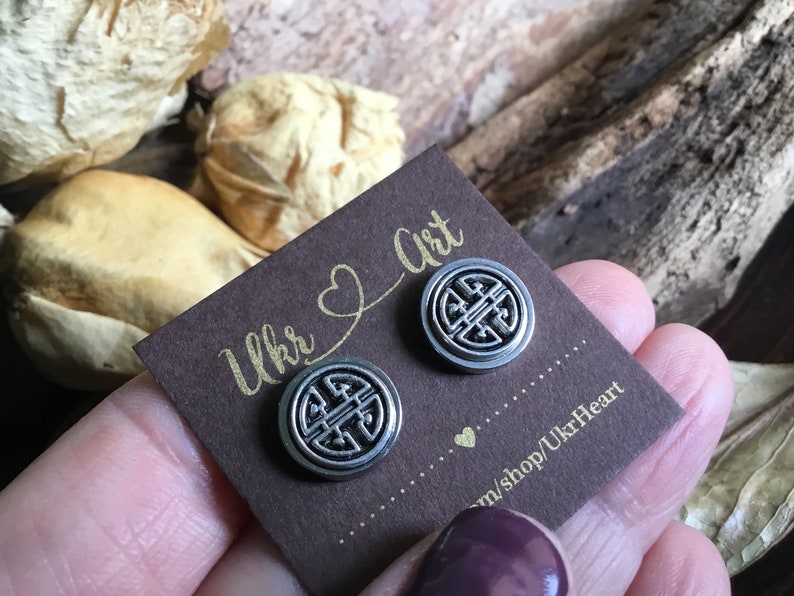 May include: A pair of silver earrings with a circular design featuring a knot pattern. The earrings are displayed on a brown card with the text "Ukr Art" and "m/shop/UkrHeart".