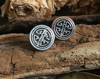 May include: Two round earrings with a black and silver design. The earrings are on a wooden surface.