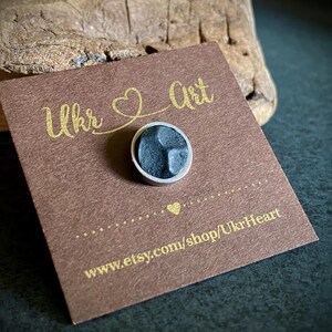 May include: A small, round, dark grey pin with a silver border is on a brown card. The card has gold text reading "Ukr Art" and "UkrHeart". The Etsy shop URL is also visible.