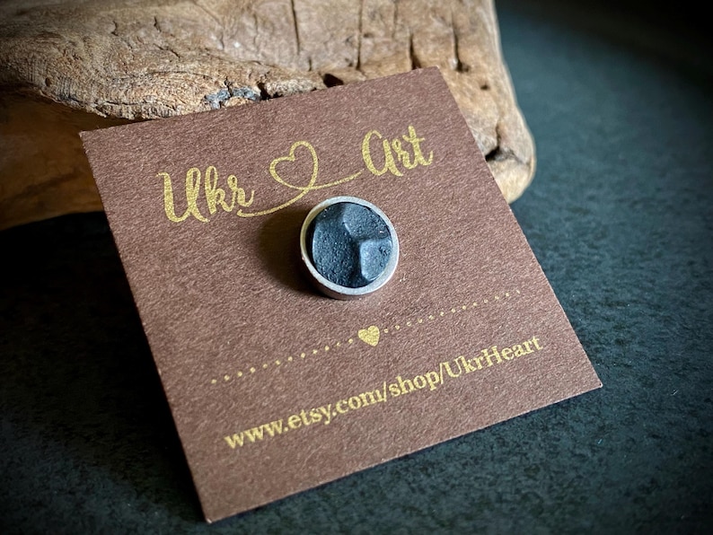May include: A small, round, dark grey pin with a silver border is on a brown card. The card has gold text reading "Ukr Art" and "UkrHeart". The Etsy shop URL is also visible.