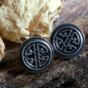May include: A pair of silver stud earrings with a black, intricate knot design. The earrings are round and have a polished finish.