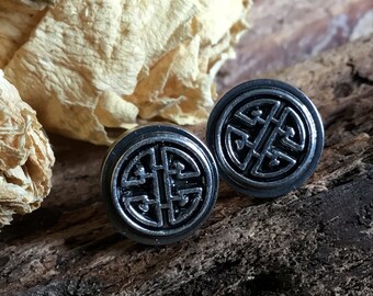 May include: A pair of silver stud earrings with a black, intricate knot design. The earrings are round and have a polished finish.