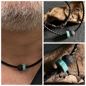 May include: A black leather necklace with a turquoise and lava rock bead. The necklace is shown on a wooden surface and on a person's neck.