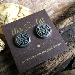 May include: A pair of silver stud earrings with a circular design featuring a stylized knot. The earrings are displayed on a brown card with the text "Ukr Art" and a website address.