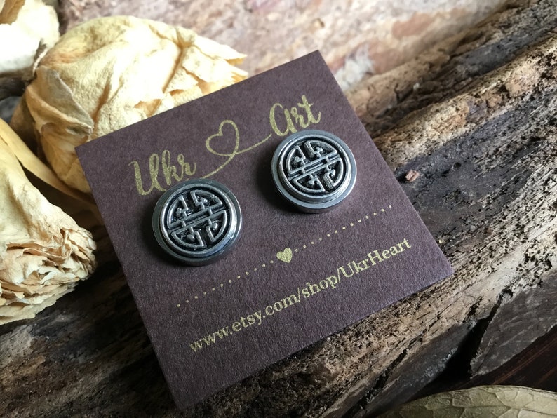 May include: A pair of silver stud earrings with a circular design featuring a stylized knot. The earrings are displayed on a brown card with the text "Ukr Art" and a website address.