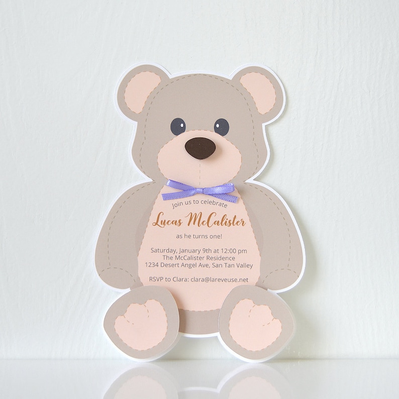May include: A teddy bear shaped invitation with a purple ribbon around its neck. The invitation reads "Join us to celebrate Lucas McCalister as he turns one! Saturday, January 9th at 12:00 pm The McCalister Residence 1234 Desert Angel Ave, San Tan Valley RSVP to Clara: clara@lareveuse.net"