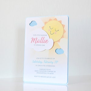 May include: A blue and yellow birthday invitation with a sun and clouds graphic. The text reads "Our little sunshine Mollie is turning one. Join us to celebrate on Saturday, February 18th at one in the afternoon. Darling Divas 8435 Castleton Corner Dr Indianapolis, IN 46250 RSVP to Megan 669.221.6251"