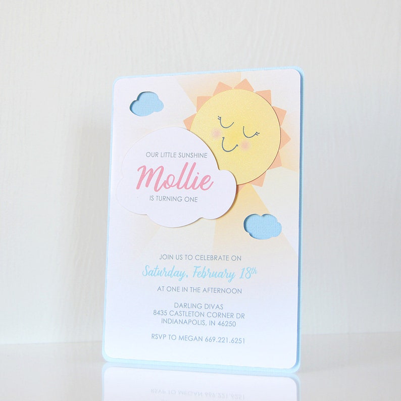 May include: A blue and yellow birthday invitation with a sun and clouds graphic. The text reads "Our little sunshine Mollie is turning one. Join us to celebrate on Saturday, February 18th at one in the afternoon. Darling Divas 8435 Castleton Corner Dr Indianapolis, IN 46250 RSVP to Megan 669.221.6251"