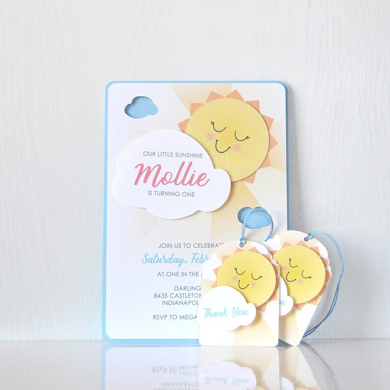 May include: A blue and yellow birthday invitation with a sun and cloud design. The invitation says "Our little sunshine Mollie is turning one." It also includes the text "Saturday, February" and "RSVP to MEGA".