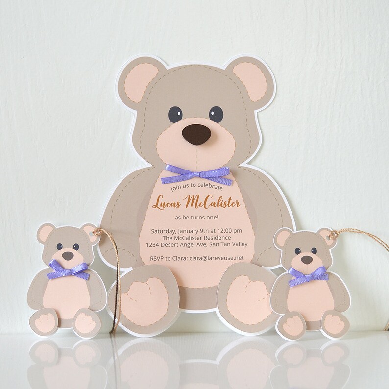 May include: A teddy bear-shaped invitation for a first birthday party. The invitation features the text "Join us to celebrate Lucas McCalister as he turns one!" with the date, time, and location of the party. The invitation is decorated with two smaller teddy bears.