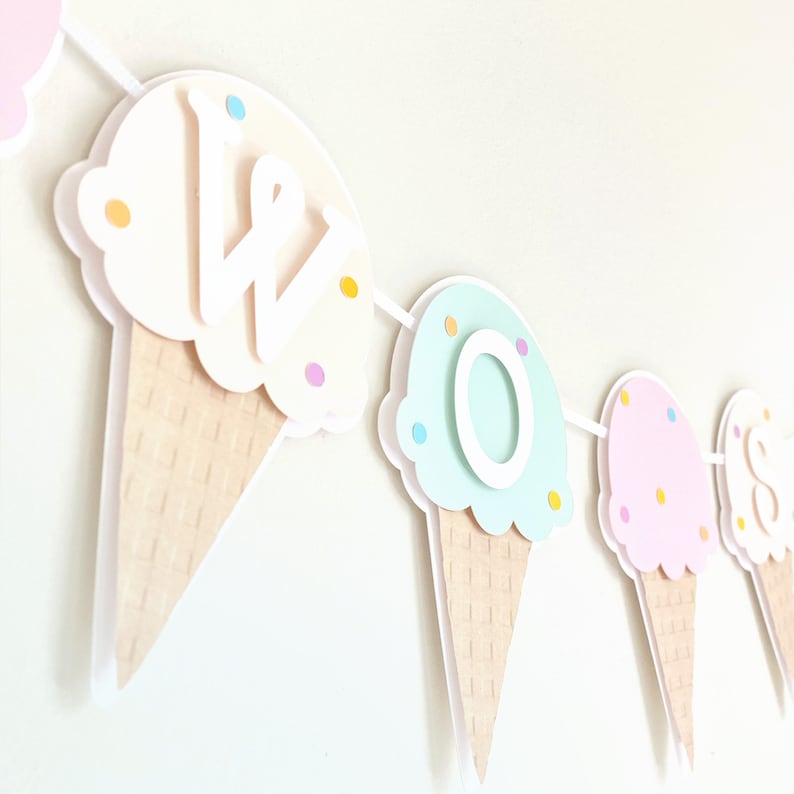 Op de afbeelding: Een kleurrijk ijshoorntje-banner met de letters "W O S" in wit. De hoorntjes zijn versierd met pastelkleurige sprinkels en de letters zijn aan de hoorntjes bevestigd.
