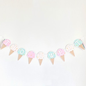 Op de afbeelding: Een pastelkleurige ijshoornbanner met de tekst "TWO SWEET". De banner is gemaakt van papier en heeft een wit touwtje erdoorheen. De ijshoorns zijn versierd met kleurrijke sprinkels.
