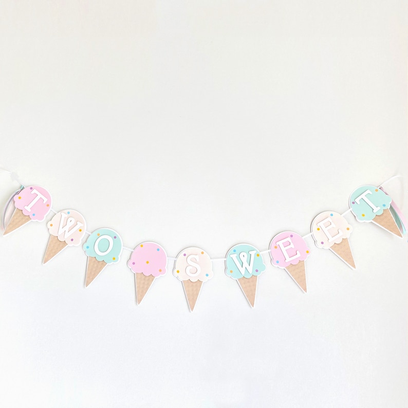 Op de afbeelding: Een pastelkleurige ijshoornbanner met de tekst "TWO SWEET". De banner is gemaakt van papier en heeft een wit touwtje erdoorheen. De ijshoorns zijn versierd met kleurrijke sprinkels.