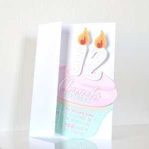 May include: A pink and blue cupcake with two lit candles that say "12" on top. The cupcake is on a white card with the text "Chanel's Birthday" and party details.