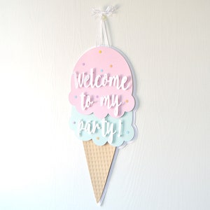 May include: A pink and blue ice cream cone shaped welcome sign with the text "Welcome to my party!" hanging from a white string.