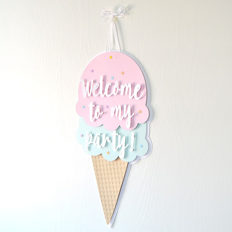 May include: A pink and blue ice cream cone shaped welcome sign with the text "Welcome to my party!" hanging from a white string.
